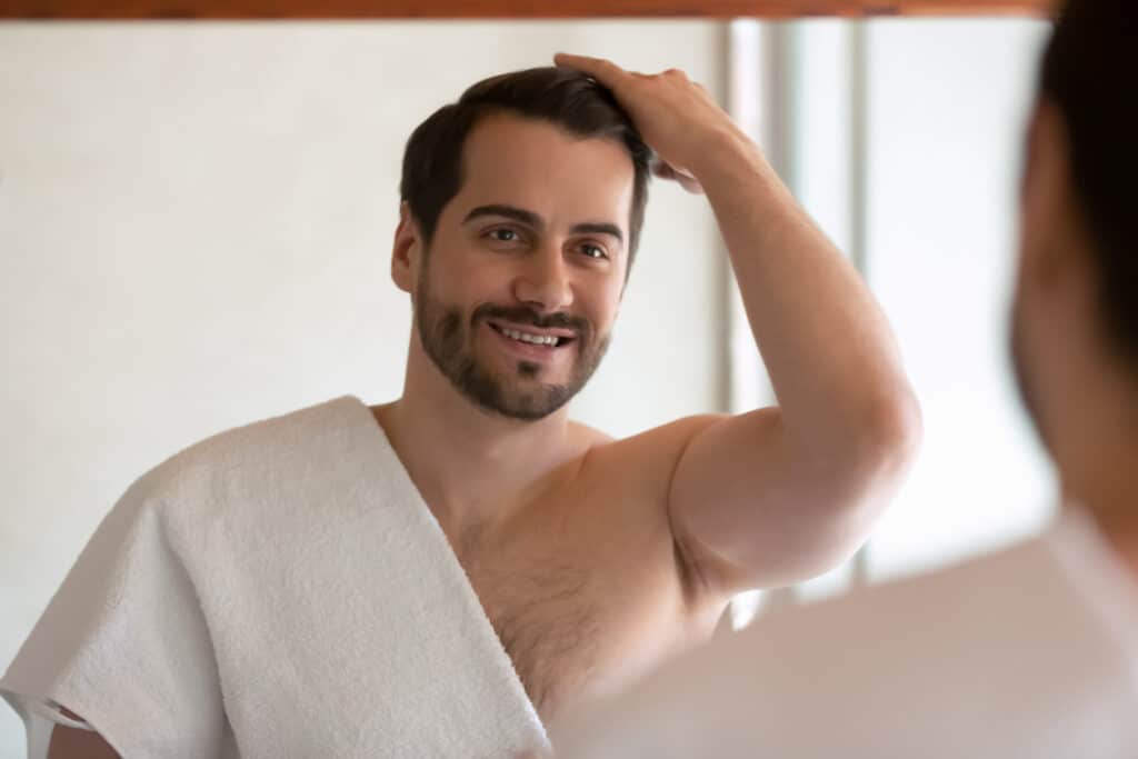 Man combing fingers through his hair while looking in the mirror