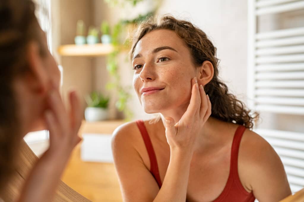 woman looking at her face in the mirror after facial scar revision procedure.