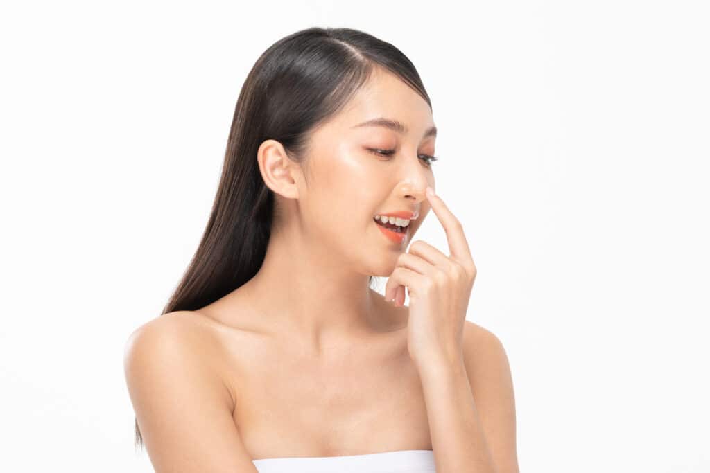 Side profile of a woman touching her nose, representing liquid rhinoplasty and surgical rhinoplasty considerations.