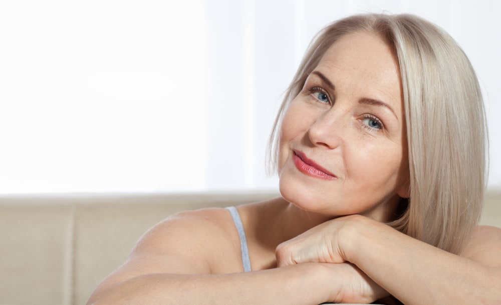 Mature woman with blonde hair smiling softly while resting her chin on her hands.